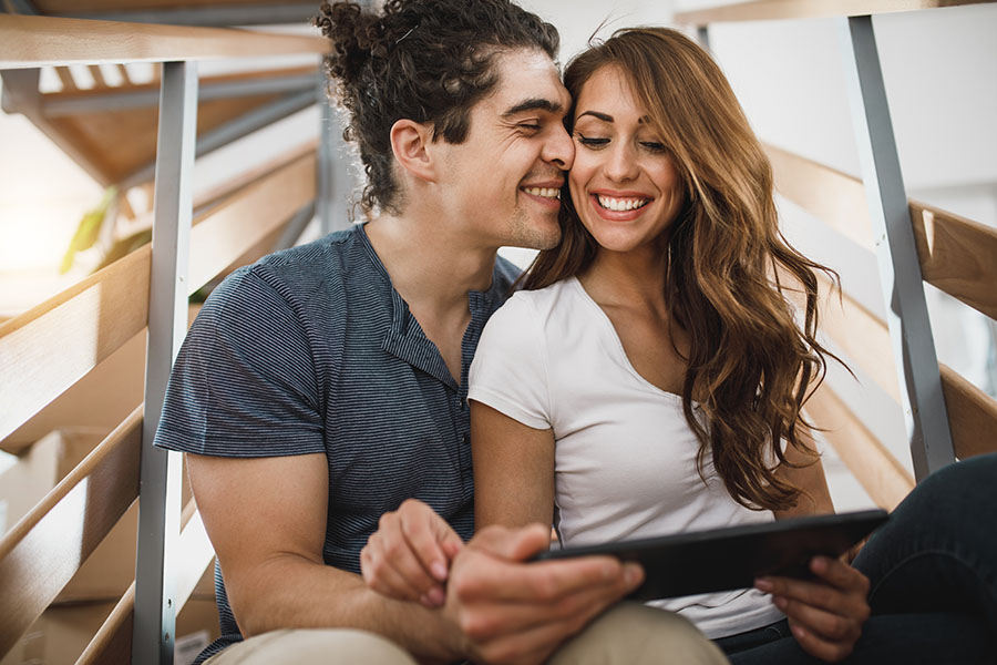 Client Center - Portrait of a Joyful Young Couple Sitting on the Steps in Their New Apartment While Using a Tablet