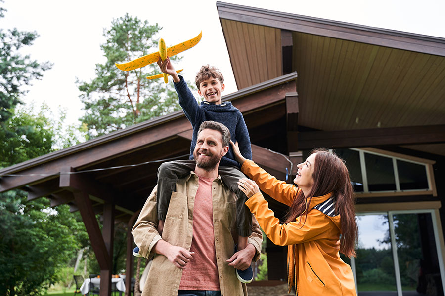 Personal Insurance - Portrait of a Happy Family Standing Outside Their Home While Playing with Their Son Who is Holding a Toy Airplane